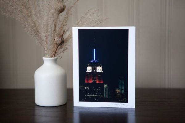 photo greeting card featuring an iconic new york city landmark he empire state building at night light up red, white and blue  photograph created by laura cook of vision photography