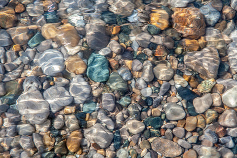 colourful turquoise and orange beach pebbles under water with the sun reflecting through the rippling waves