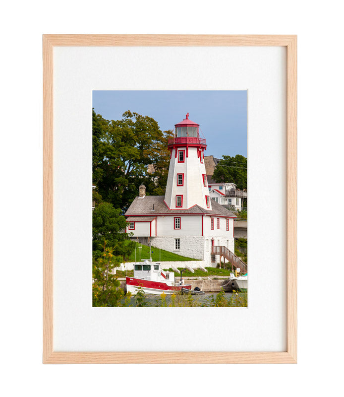 A vertical photograph of the historic white and red Kincardine Lighthouse in Ontario, featuring a matching red and white fishing boat docked in the foreground under a clear blue sky.