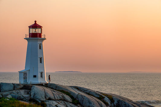 Fine art photography of Peggy’s Cove Lighthouse at sunset, featuring golden light on granite rocks and a purple Atlantic sky.

