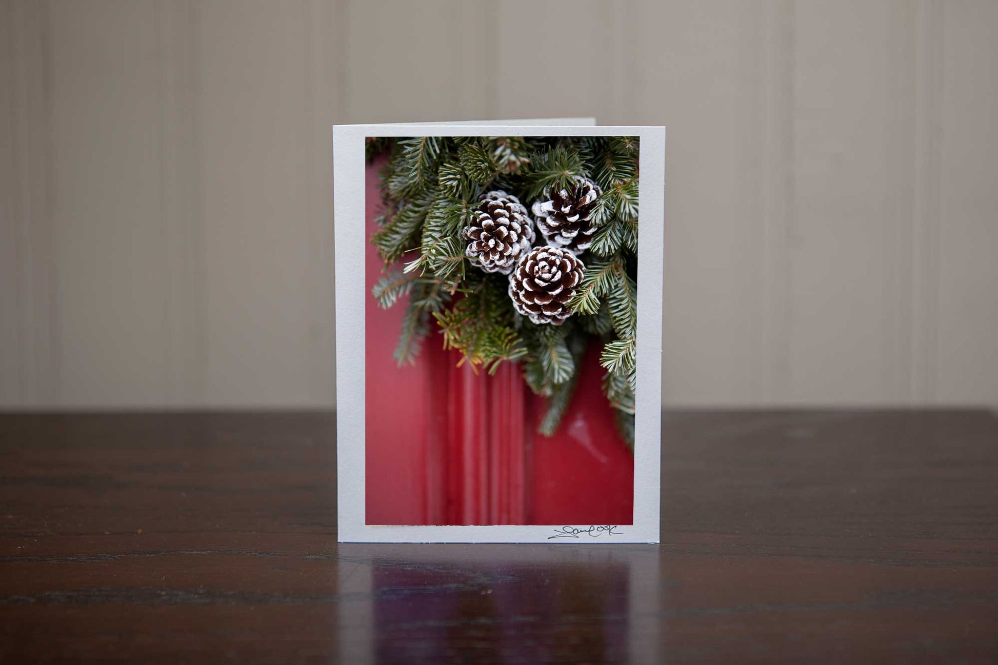 Greeting card featuring 'Adorn' a photograph of a red door with close up of a Christmas wreath of evergreen trees and pinecones on the door Photo by Cambridge Ontario Photographer Laura Cook of Vision Photography