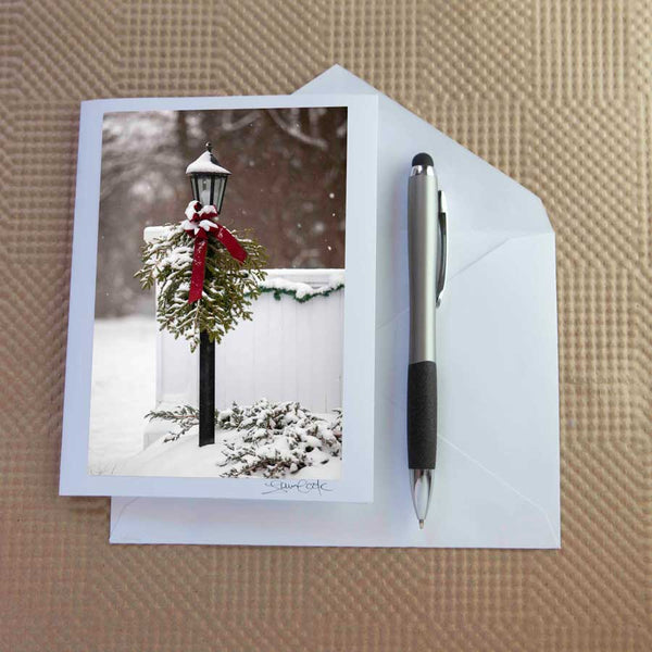 Christmas card pack of wintery scenes by Laura Cook / Vision Photography features a photo of a lamp post covered in a wintry bough with a red velvet bow 